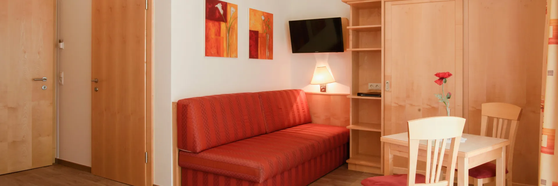 Hotelzimmer mit einer roten Couch und einem charmanten Holzesstisch für zwei Personen.