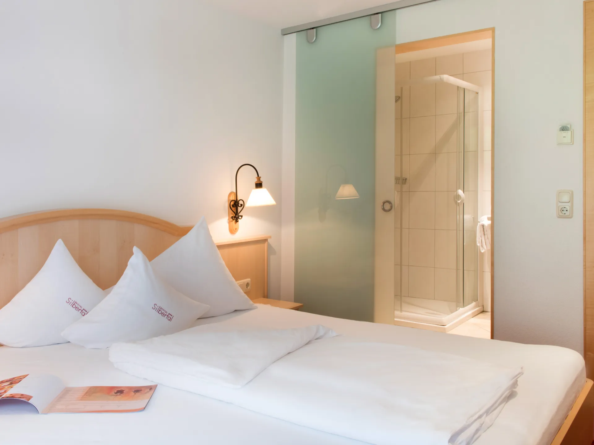 Hotel-Einzelzimmer mit Blick auf die Dusche, die durch eine stilvolle Glasschiebetür abgetrennt ist.