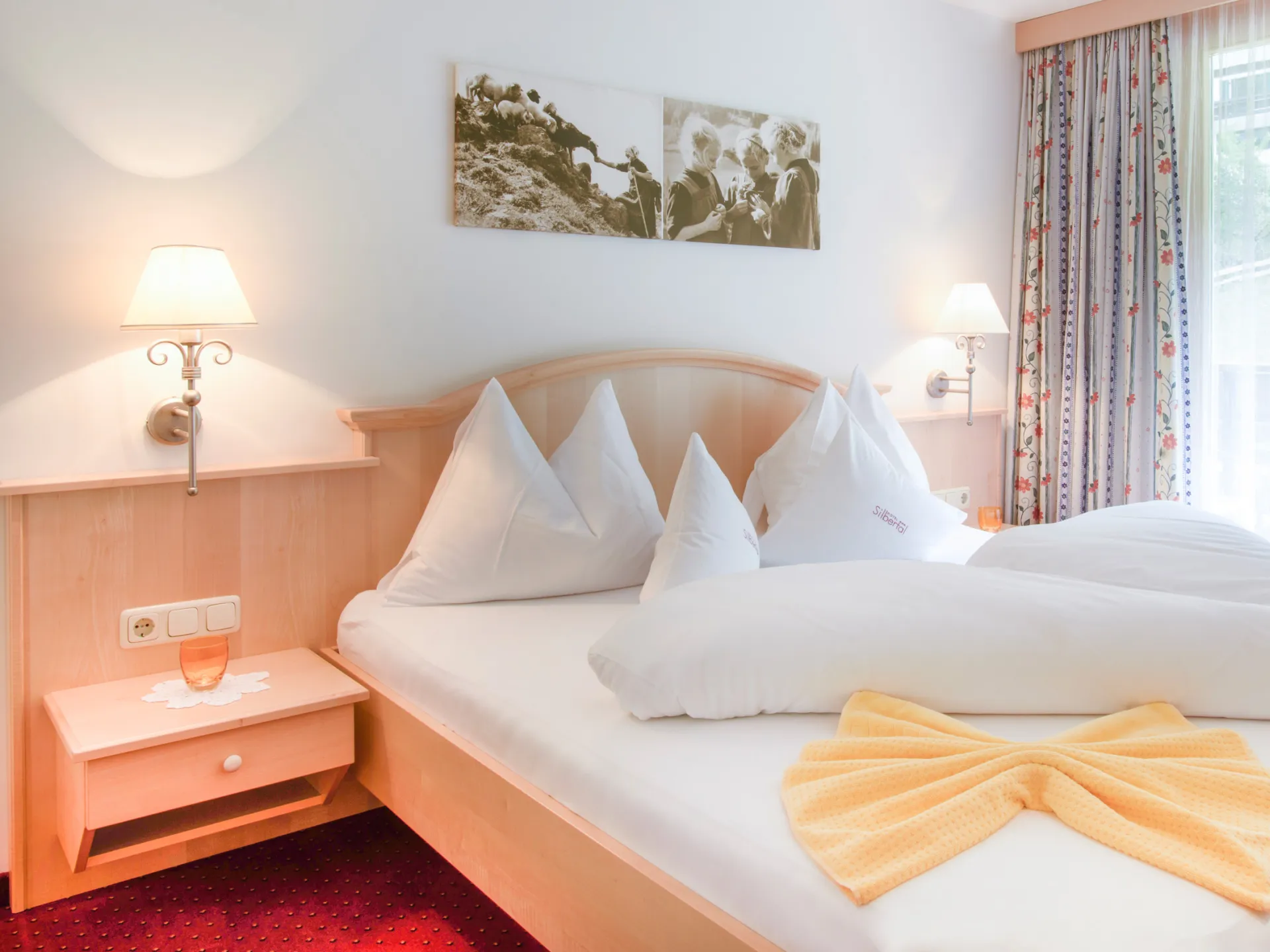 Schön gemachtes Doppelbett in einem Hotelzimmer mit gelben Elementen auf dem Bett. 