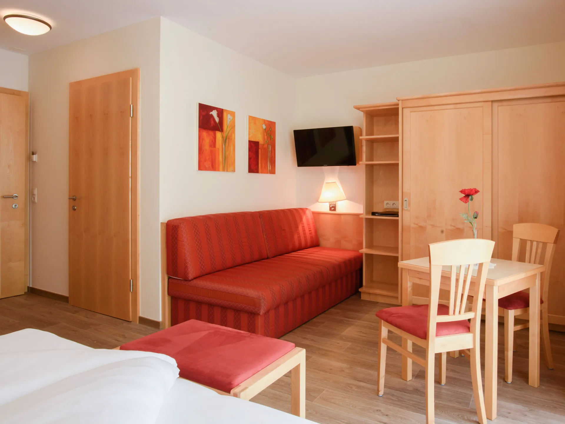 Hotelzimmer mit einer roten Couch und einem charmanten Holzesstisch für zwei Personen.
